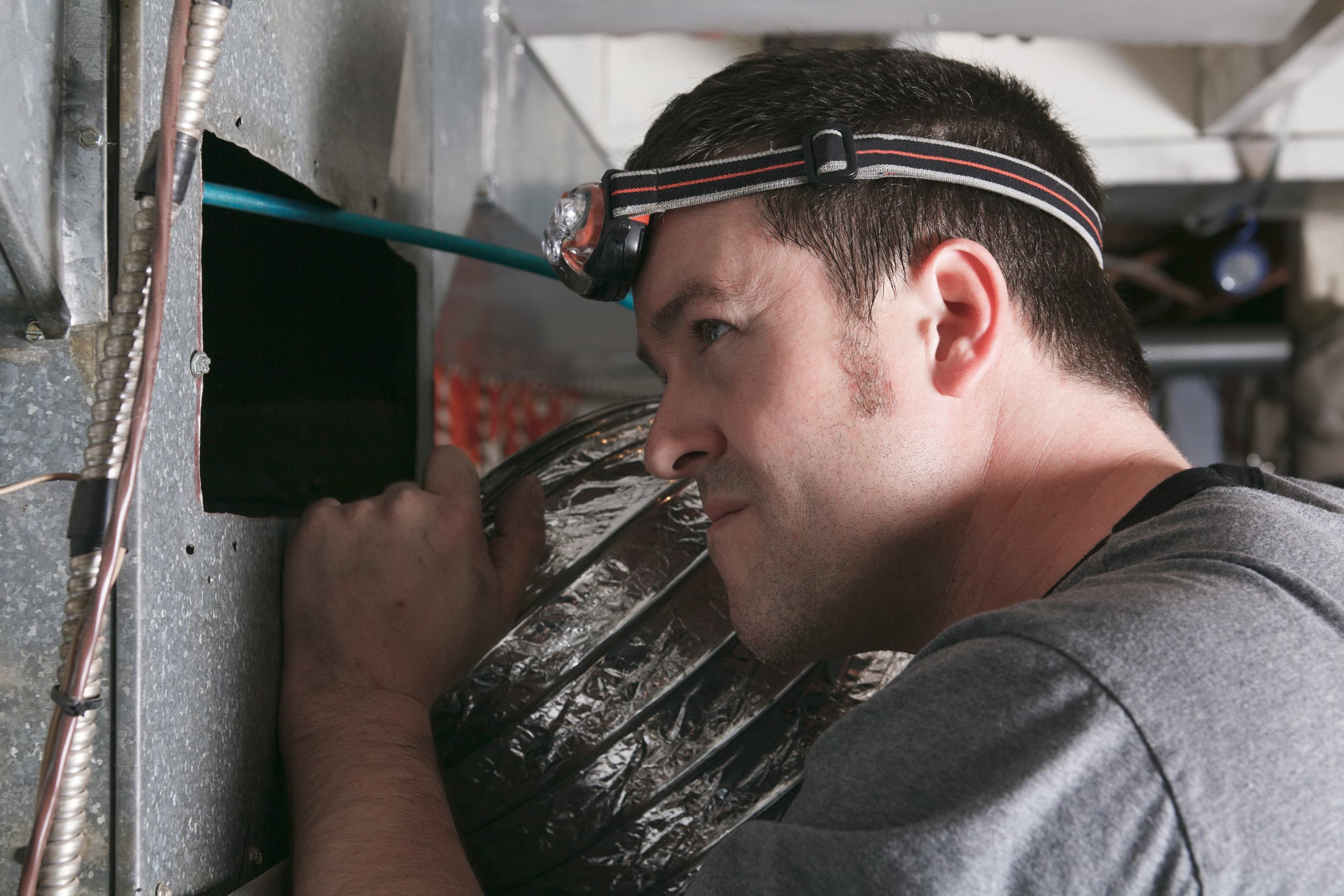 closeup of a technician carefully inspecting an air duct entrance in order to perform repairs