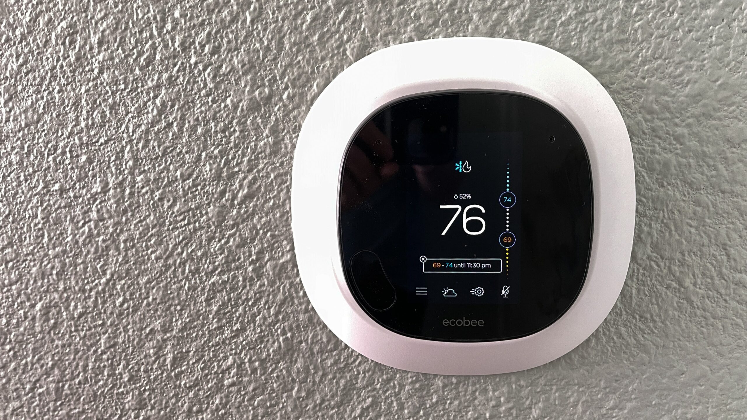 closeup of a smart thermostat positioned on a wall sitting at 76 degrees and showing other system settings